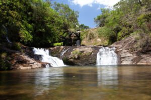 Vista frontal da Cachoeira da Pedra Furada com várias quedas d’água cercadas por vegetação e poço de águas cristalinas.