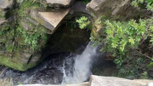 Vista superior da queda da Cachoeira da Pedra Furada, com água descendo entre rochas e vegetação densa ao redor.