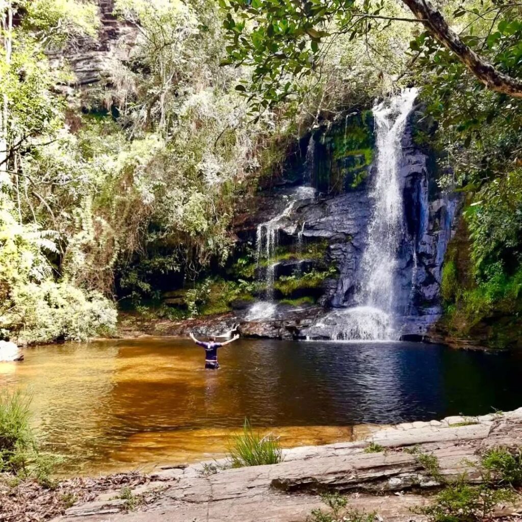 Vista panorâmica da Cachoeira da Serra Grande, evidenciando o poço de águas cristalinas e a pequena faixa de areia iluminada pelo sol.