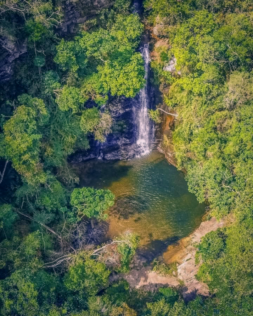 Cachoeira da Serra Grande em Luminárias, MG, com sua queda d'água de 12 metros cercada por vegetação exuberante.
