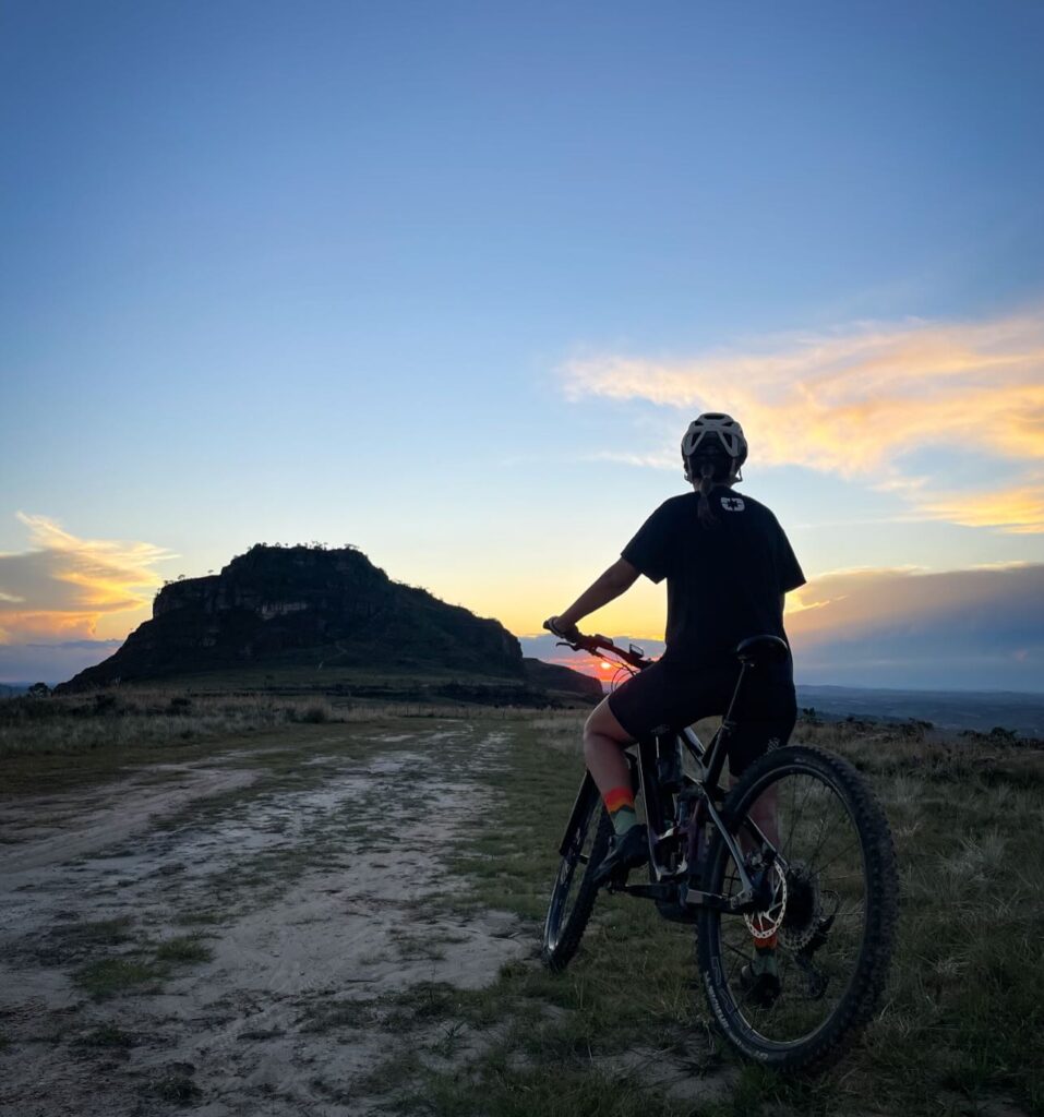Visitante de bicicleta no Pico do Cruzeiro apreciando a vista panorâmica das montanhas e vales de Luminárias.​