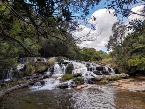 Caminho de água descendo em degraus naturais entre pedras lisas, rodeado por mata preservada.